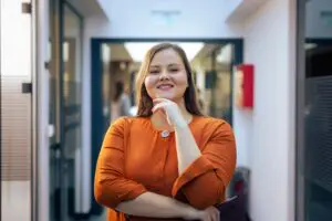 Woman in orange shirt standing confidently indoors.